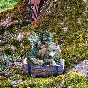 Close-up of fairy girl and white wolf figurine among garden moss and tree roots