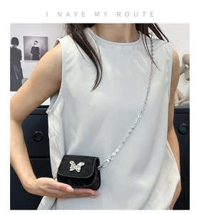 Detail of a mini black velvet saddle bag with a silver butterfly charm and metal chain