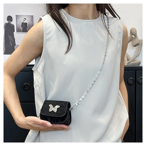 Detail of mini black saddle bag with silver butterfly charm and metal chain strap
