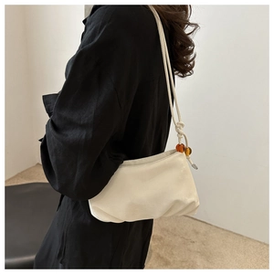 Détail du sac à bandoulière crème avec fine lanière et perles décoratives en ambre