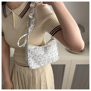 Detail view of floral underarm bag featuring ruffled shoulder strap and zip closure