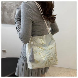 Detail of bamboo leaf embroidery on a cream shoulder bag with a tassel charm