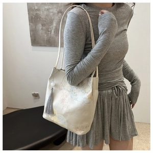 Detail of elegant beige tote bag with floral patterns and a gray tassel pendant