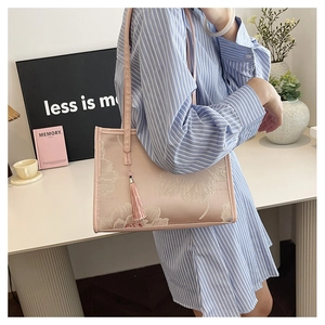 Detailed embroidery of white flowers on a pink tote bag with elegant tassel charm