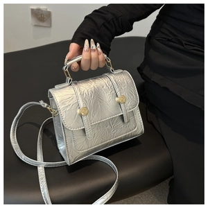 Gros plan sur la texture plissée argentée et les boucles dorées d'un sac à rabat