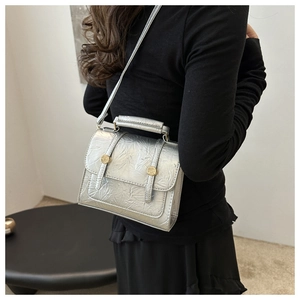 Détail du sac à main argenté métallisé avec texture et boucles dorées porté par un mannequin