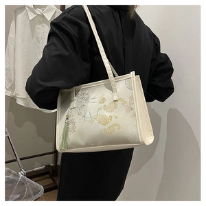 Detailed embroidery texture on ivory brocade bucket bag with green tassel charm