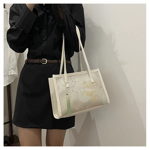 Detail of floral embroidery and green silk tassel on a white chinoiserie tote bag