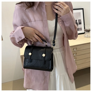 Détail du sac noir texturé avec boucle dorée sur mannequin dans un intérieur chaleureux