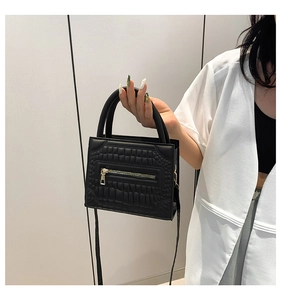 Detail of black faux leather handbag with crocodile pattern and gold zipper accents