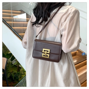 Détail d'un sac bandoulière en cuir mat marron foncé avec boucle dorée géométrique