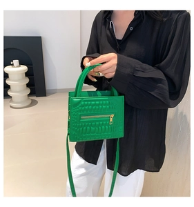 Detailed view of the bright green crocodile texture leather handbag with gold zipper detail