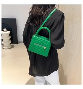 Detail of bright green crocodile embossed handbag with gold zipper and shoulder strap