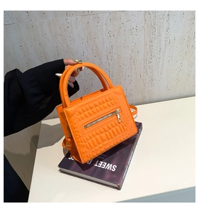 Detail of vibrant orange textured handbag with metal zipper and rigid top handle