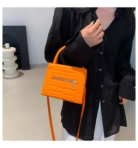 Detail of orange crocodile pattern crossbody bag with metallic zipper and top handle