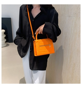 Detail of orange crocodile pattern handbag featuring gold zippers and adjustable shoulder strap