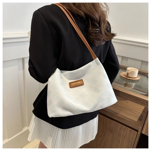 Detail of blue textured tote bag with brown leather straps shown on a model's shoulder