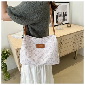 Detail of woven tote bag featuring a leather logo patch and thin brown shoulder straps