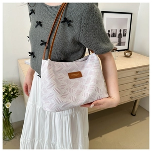 Close-up of pink woven shoulder bag with brown leather strap in a minimalist interior setting