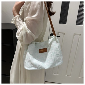 Detail view of light green woven tote bag with brown leather handles and brand logo tag