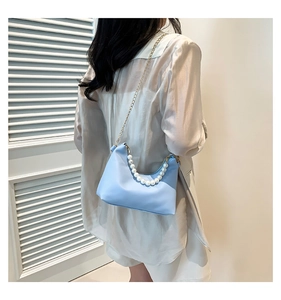 Detail view of light blue crescent bag with pearl handle and golden chain shoulder strap