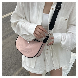 Pink crescent shoulder bag with wide black strap shown on a model in a street style shot
