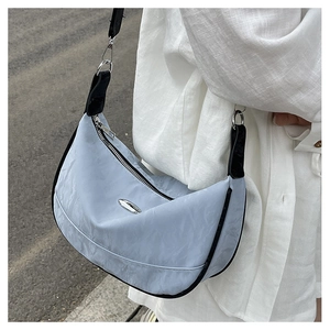 Detail view of light blue half-moon crossbody bag with wavy texture and silver metal plaque