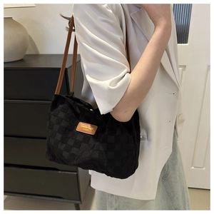Détail du sac cabas à damier noir avec anses en cuir marron et plaque logo dorée