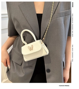 Detail view of mini white PU leather square bag with golden bow ornament on gray blazer