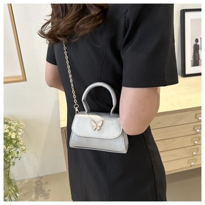 Detail of silver mini crossbody bag featuring a golden butterfly clasp and elegant chain strap