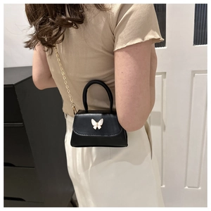 Mini black crossbody bag with white butterfly detail shown on a model's outfit