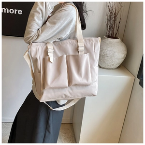 Detail of a beige tote bag with front pockets and adjustable strap in a lifestyle setting