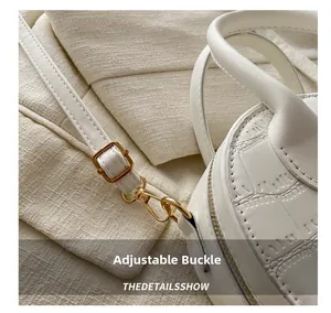 Detailed macro view of the gold adjustable buckle and crocodile pattern on the white bag
