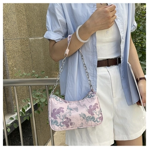 Detail of pink embroidered handbag with floral patterns and silver chain on model