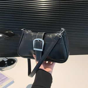 Minimalist black leather baguette bag with large silver buckle in a hand-held display