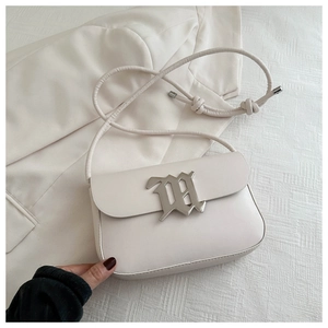 Close-up of cream shoulder bag featuring silver gothic M buckle and knotted rope strap