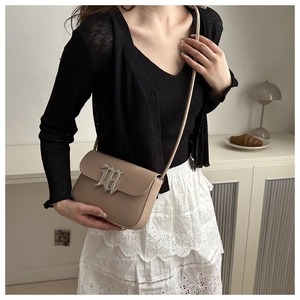 Close-up of beige shoulder bag with a large metallic M buckle and smooth leather texture
