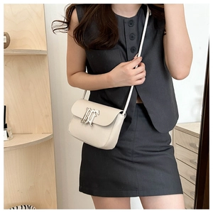 Cream white small crossbody bag with silver buckle worn by a model in a cozy interior