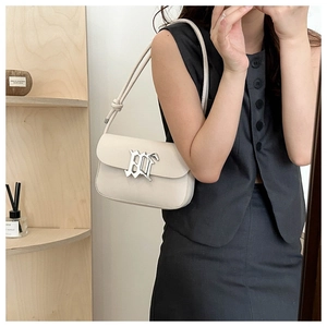 Detail of minimalist cream leather underarm bag featuring silver gothic B logo and knot strap