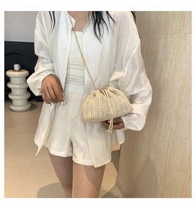 Detail of a cream woven drawstring crossbody bag with a delicate gold chain strap
