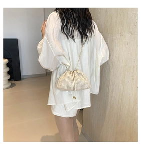 Detail of beige woven bucket bag with gold chain strap worn by a model in white