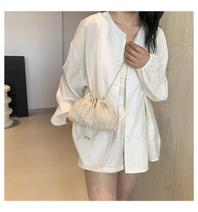 Detail of cream woven bucket bag with gold chain strap and drawstring on white outfit