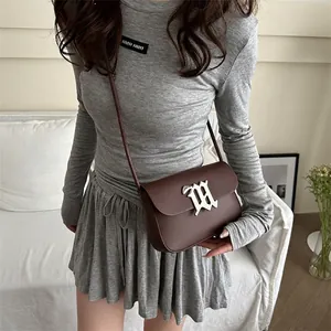 Dark brown leather shoulder bag with silver M-shaped metal buckle on white sofa