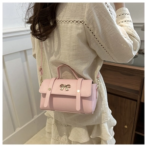 Detail view of light pink crossbody bag with golden bow ornament and top handle