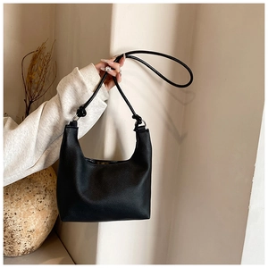 Détail de la texture grain litchi noir et de la bandoulière nouée élégante sur le sac