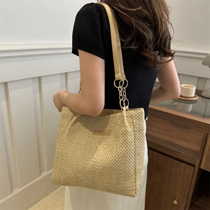 Bolso tote de tejido beige con correa de cadena metálica en un ambiente interior cálido