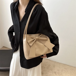 Sac fourre-tout en cuir beige avec grand nœud décoratif porté à l'épaule par un mannequin