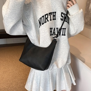 Sac bandoulière hobo noir en similicuir grainé porté par un mannequin en tenue décontractée