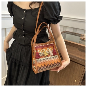 Dettaglio borsa a secchiello boho con nappe colorate e trama intrecciata su modella