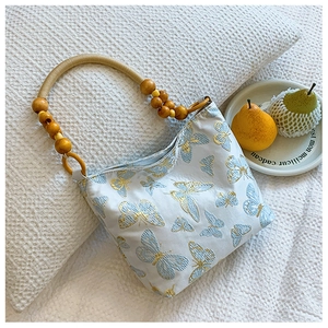 Close-up of butterfly embroidery on fabric tote bag with elegant wooden bead handle